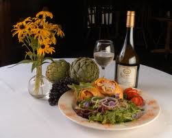 Table set with white table cloth, plate of salad, glass of wine, and a bottle of wine