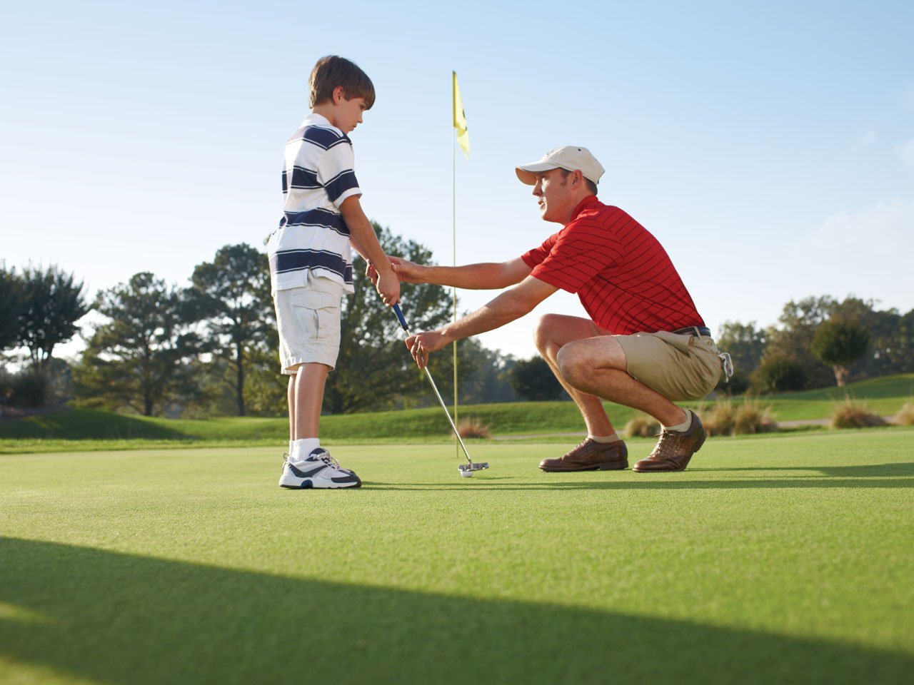 A father bending down to teach his son to golf