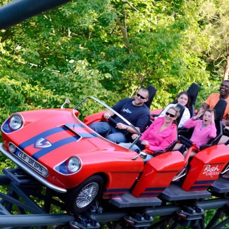 A roller coaster that looks like a red race car with people enjoying the ride
