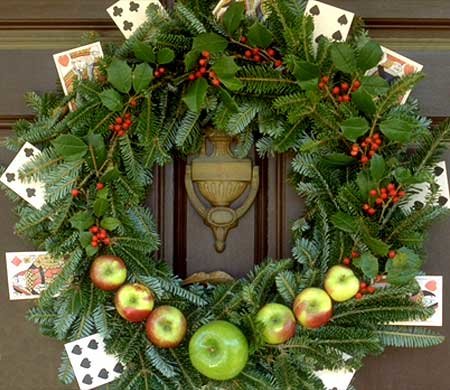 Christmas wreath hanging on a door with apples and playing cards decorating it