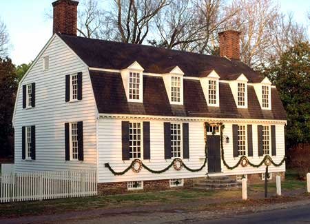 Two story while colonial home with black shutters, black door, and white picket fence decorated for Christmas
