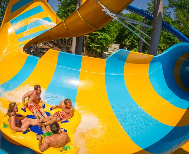 Three men and a woman enjoy a ride on a yellow raft down the Collasal Curl At Water Country Williamsburg