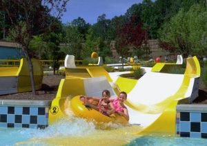 Yellow and white water slide with two young girls floating down on a yellow raft