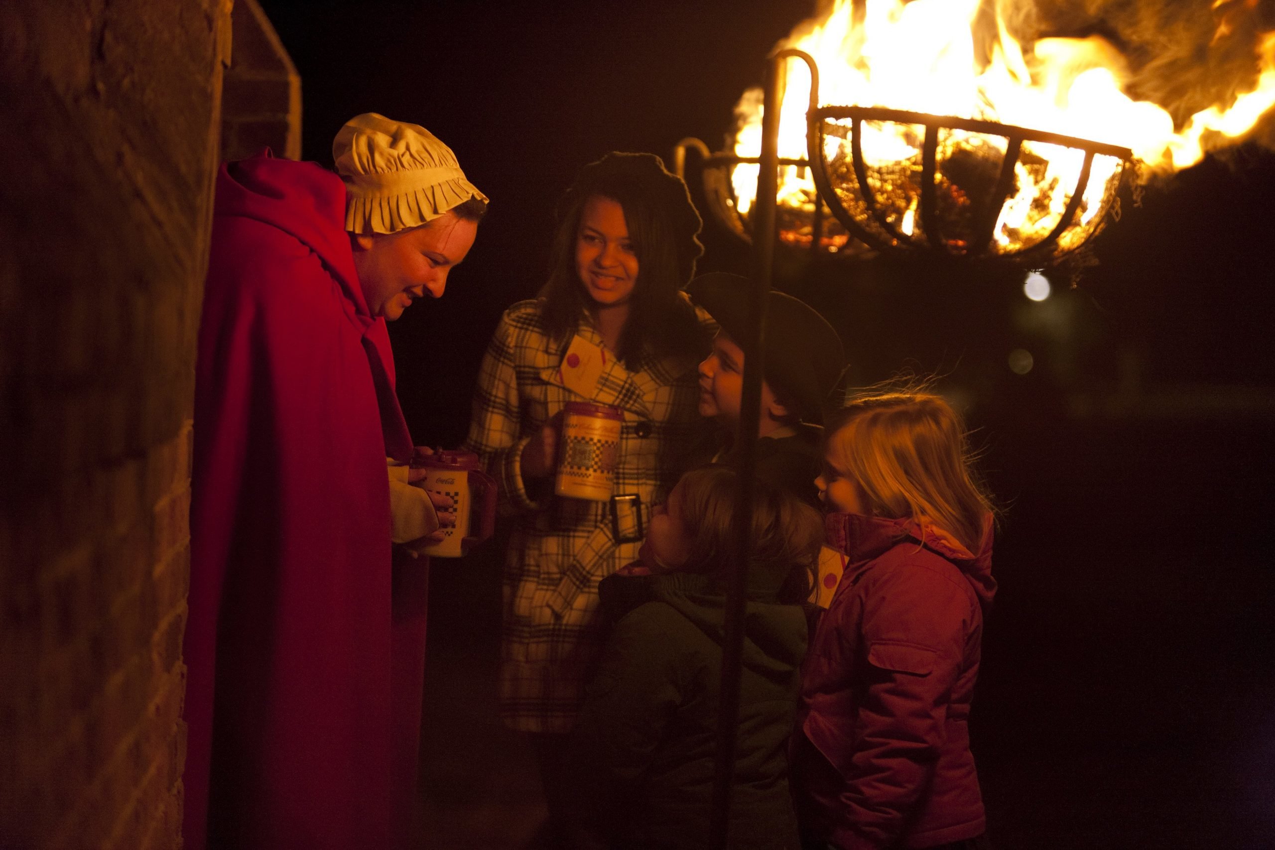 Four children drink hot chocolate next to a fire and talking with a woman in character