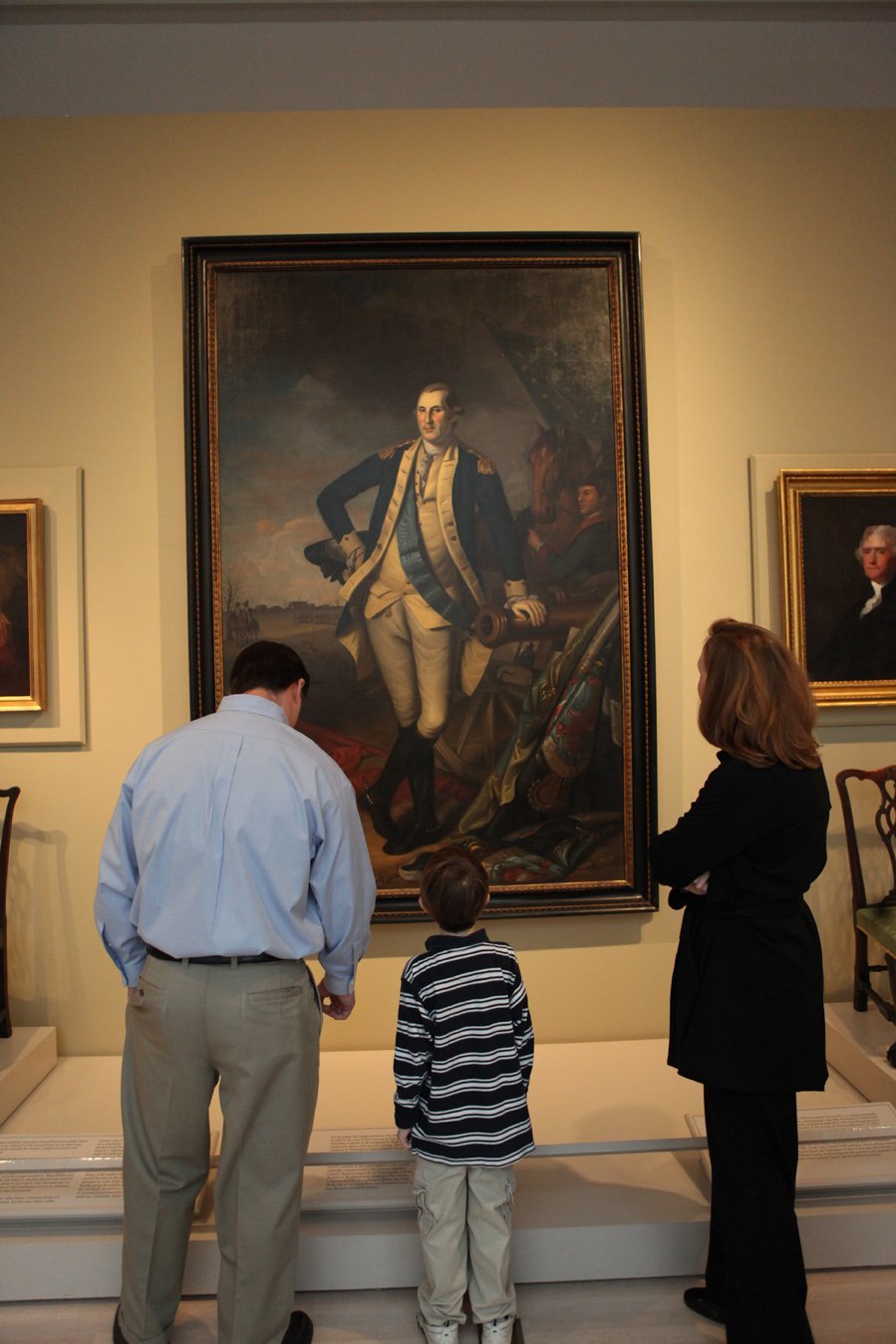 A man, child, and woman standing in front of a painting at a museum