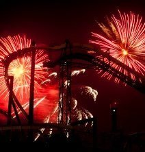 Red fireworks at night behind a large roller coaster