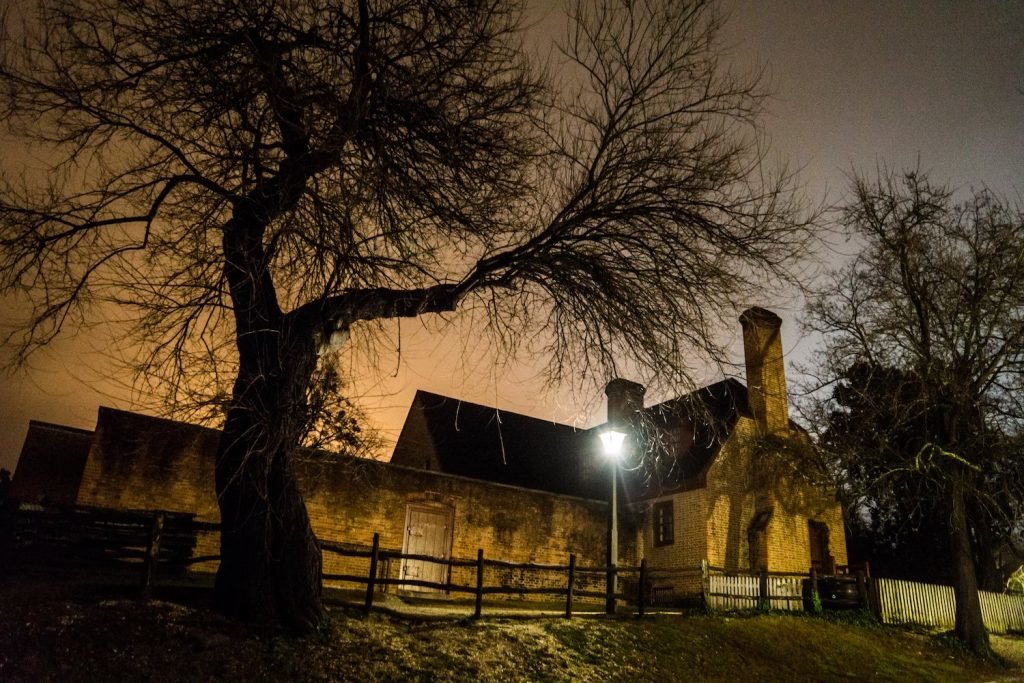 House at dusk with wooden fence in front of it and spooky looking tree